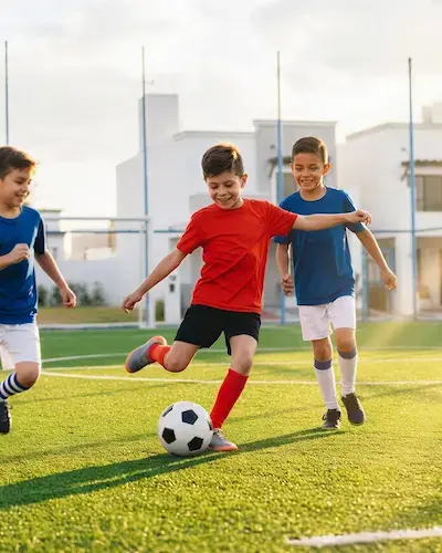 Tres niños jugando fútbol en la cancha de pasto sintético